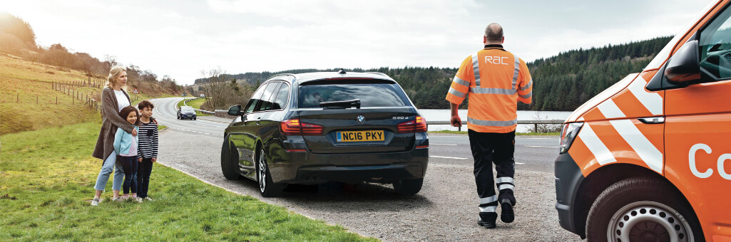 RAC patrol walking towards the back of the car with a family to the left